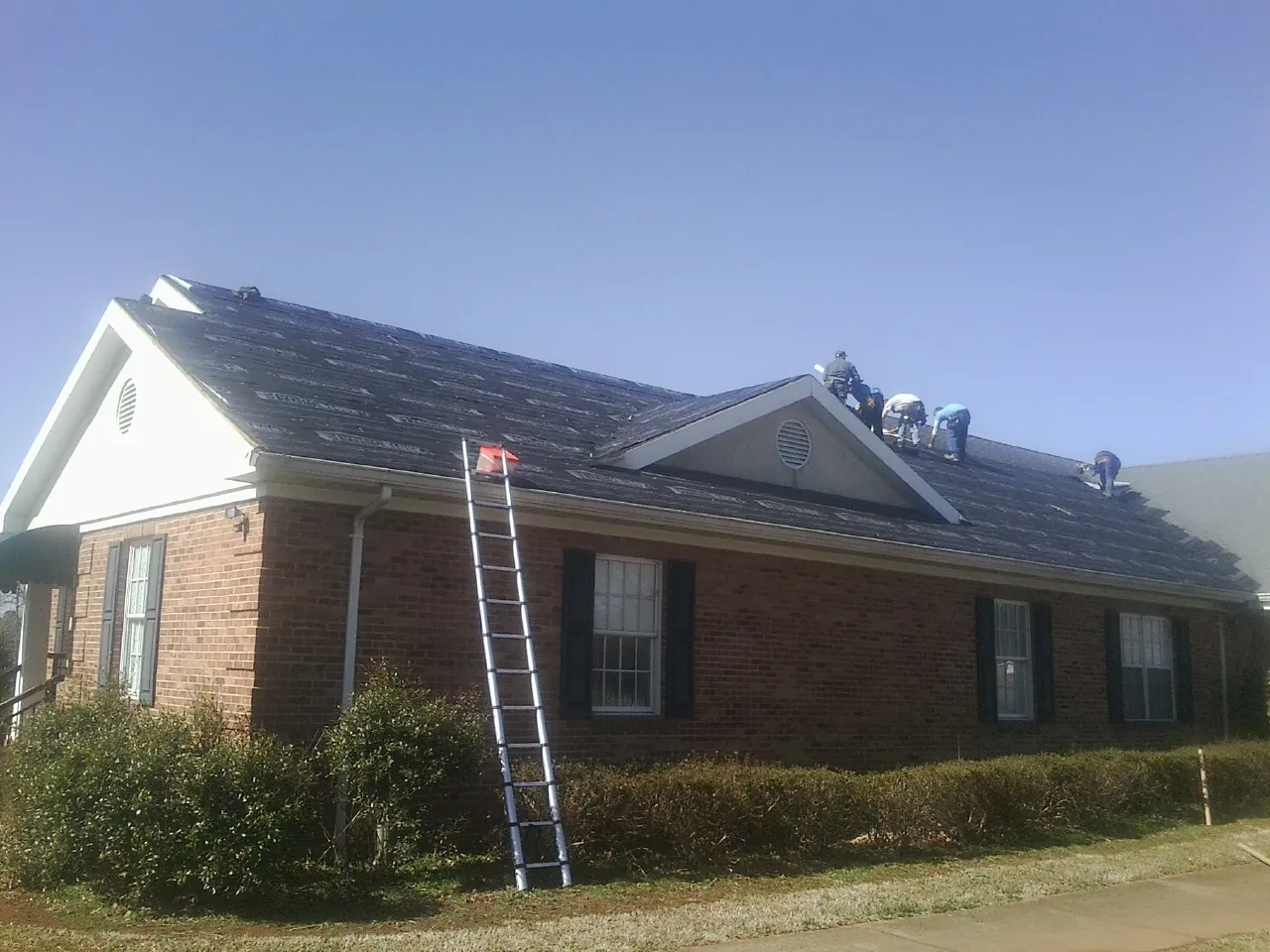 Crew tearing shingles off a brick ranch roof with a ladder set — Emergency Roof Repair work by our crew in Hawk Run