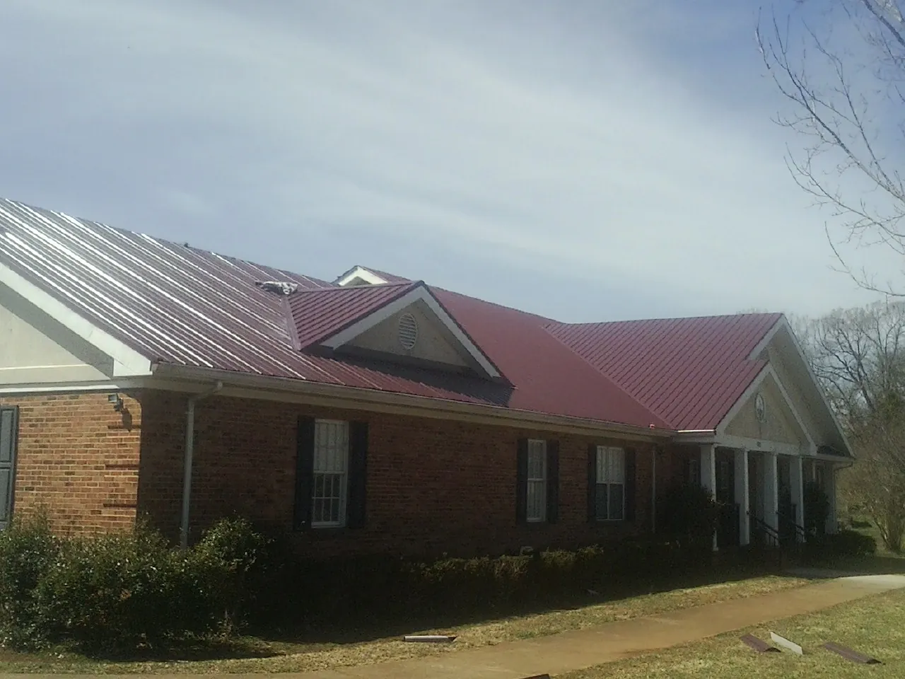 Red metal roof with gabled entries on a long brick building, from a Hail Damage Roof Repair job in Hawk Run