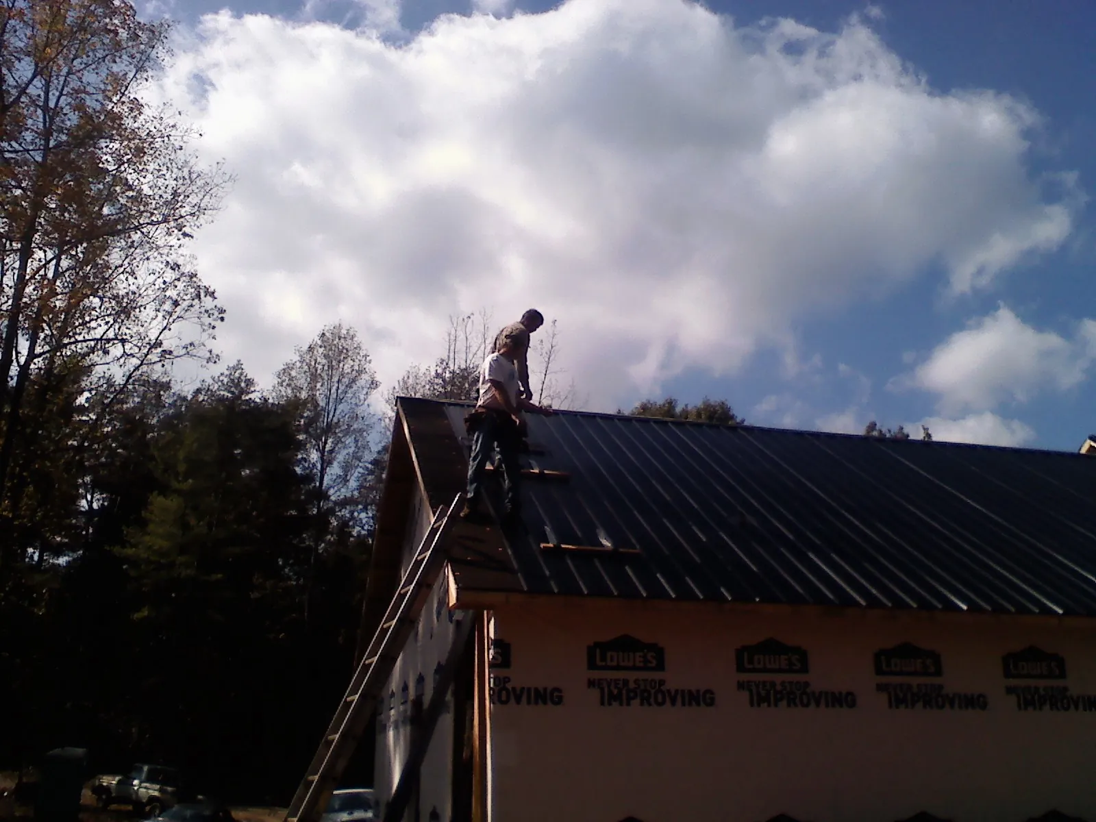Roofer fastening dark metal panels high against a cloudy sky, from a Roof Inspection job in Hawk Run