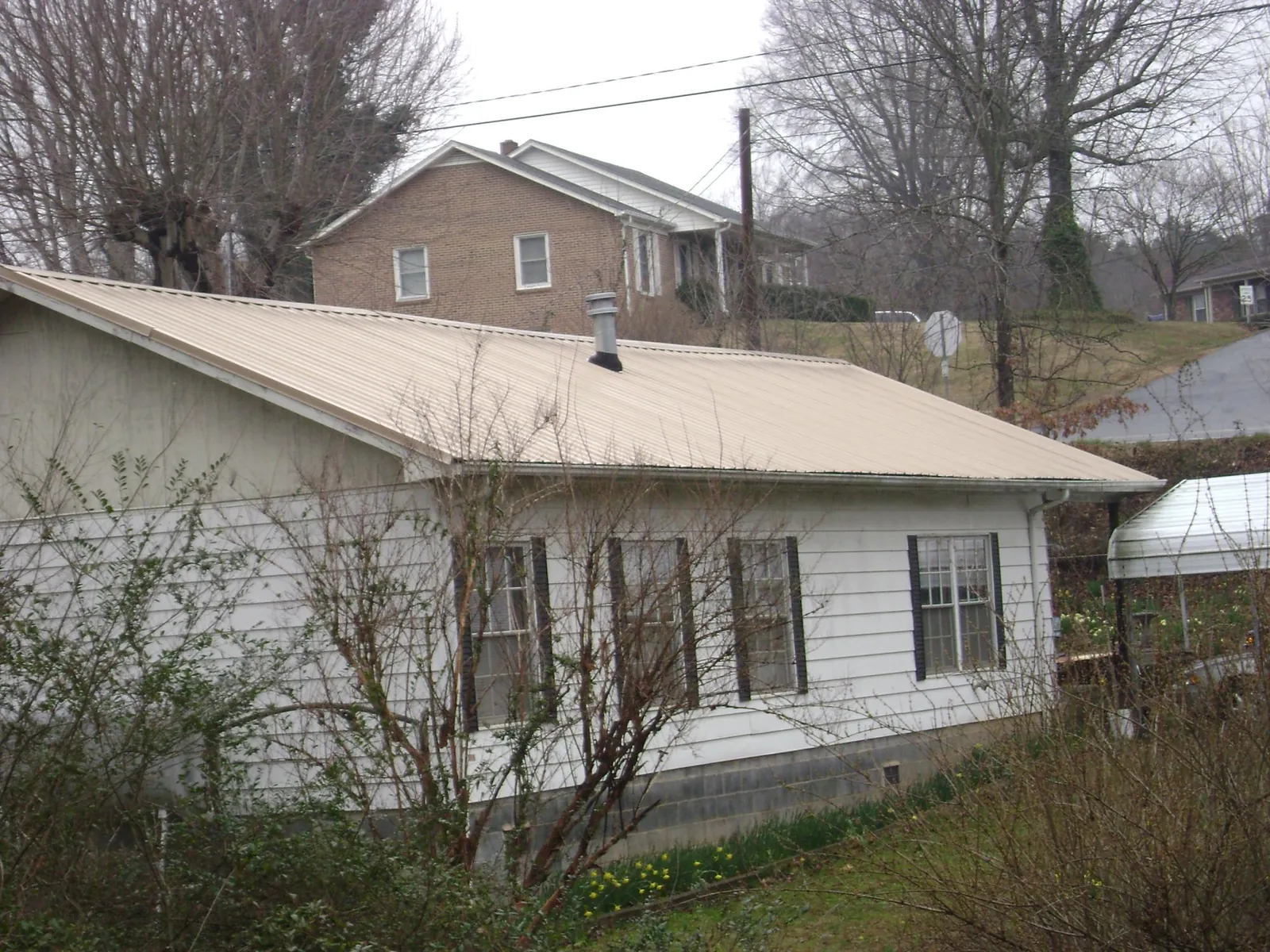 Tan metal roof on a white sided house set into a hillside — Commercial Roofing by Roofing Brothers in Hawk Run
