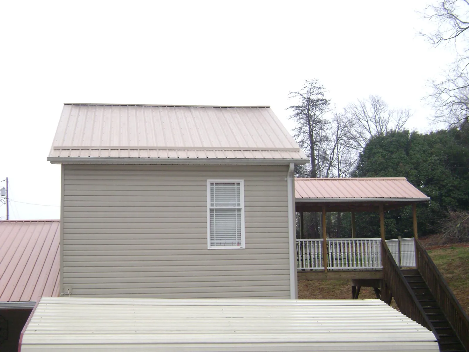 Tan metal roofs on a two story addition and attached porch, from a Roof Replacement job in Hawk Run